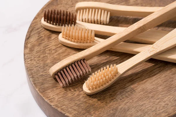 Tahta tepside beyaz mermer masa arkasında doğal kıllı bambu diş fırçalarının yakın görüntüsü. Model, seçici odak