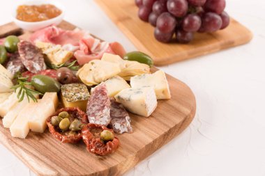 Geleneksel İtalyan aperatifi, peynirli pansiyon, güneşte kurutulmuş domates, zeytin, beyaz masa üzerinde üzüm ve reçel ile servis edilen sosisler - parmesan, gorgonzola, prosciutto, salam. Peynir ve et çerezi tabağı.
