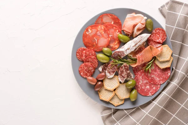 Farklı mezeler, farklı türde sosis tabakları - salam, bresaola, zeytin, biberiye ve kraker ile servis edilen proscuitto. Beyaz masa arkasında geleneksel İtalyan antipasti ve fotokopi alanı olan gri tabak.