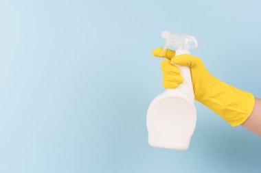 Sarı koruyucu lastik eldiven, elinde deterjan şişesiyle mavi arka planda fotokopi alanı olan bir eldiven. Farklı mutfak ve banyo yüzeyleri için temizlik malzemesi. Çamaşır suyu. Model