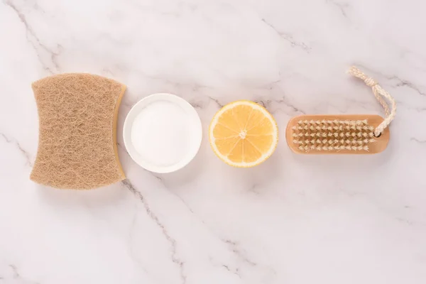 Flat lay composition with natural household cleaners kit with eco ingredients - bamboo brush, lemon, baking soda, citric acid on marble background. Green cleaning concept, selective focus