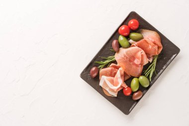 Siyah şarküteri tahtasında beyaz beton masa zemininde fotokopi alanı olan zeytinlerle servis edilen üst manzara. Geleneksel İtalyan antipastasıyla siyah tabak, İtalyan aperatifi.