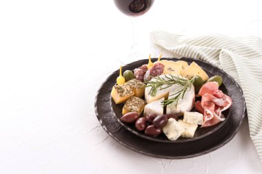 Peynir, salam ve jambonlu şarküteri tahtası yanında zeytin ve beyaz masa arkasında bir bardak kırmızı şarap. İtalyan geleneksel pastası.
