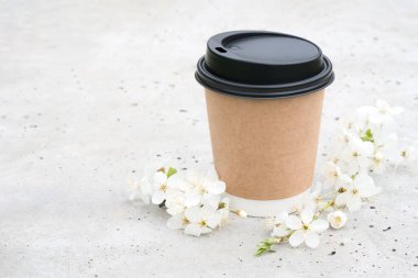 Beton zemin üzerinde plastik kapaklı kahverengi Kraft kağıt kahve fincanı ve etrafında çiçek açan kiraz ağacı brunch 'ları. Şablon, biçimlendirme resmi, kopyalama alanı