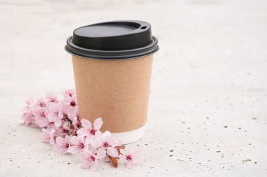 Kahverengi Kraft kağıt kahve fincanının maketi beton masa üzerinde plastik kapaklı ve etrafta çiçek açan sakura brunchları. Şablon, boşluğu kopyala
