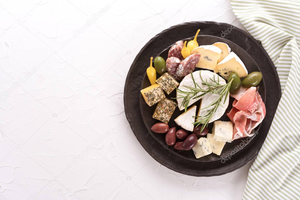 Charcuterie board with assortment of cheeses, salami and prosciutto served with olives on black plate on white table background. Italian traditional antipasti, top view