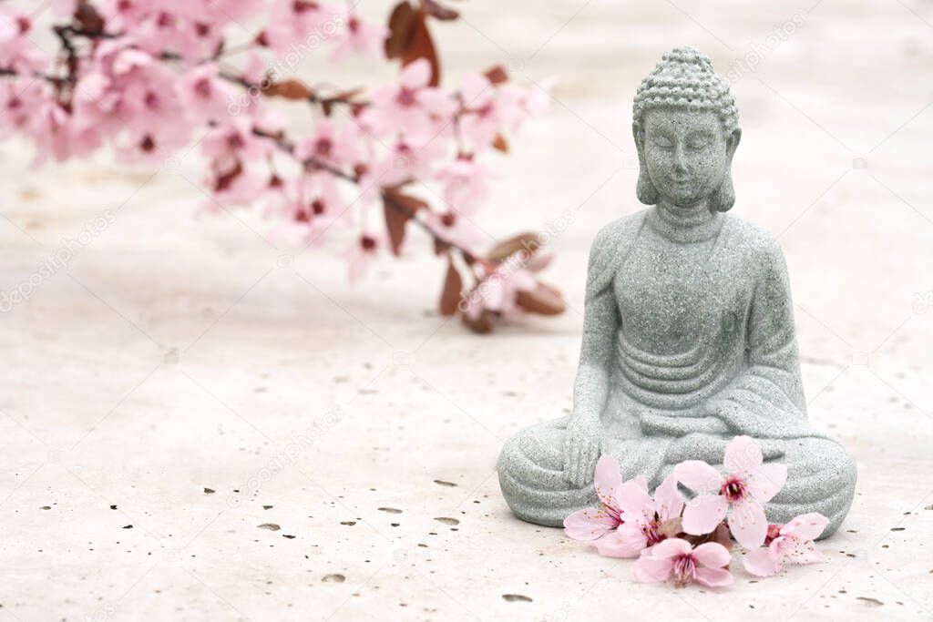 Small Buddha statuette with blooming sakura flowers on concrete background with copy space. Meditation and spa concept, mental health. Time for yourself
