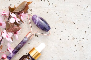 Yüz masajı kitinin yakın görüntüsü - ametist gua sha yüz silindiri ile güzellik yüz serumu ya da taş beton arka planda çiçek açan sakura dallı kozmetik yağ. Doğal taş yüz masaj aleti, boşluğu kopyala