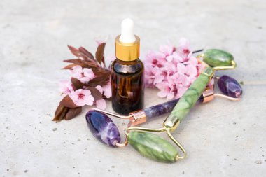 Yüz masajı seti - ametist ve yeşim taştan arkaplanda sakura dallı kozmetik yağıyla güzellik yüz silindiri. Doğal taş yüz masajcısı, model. 