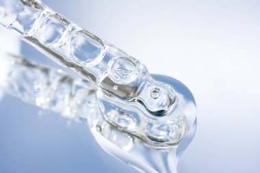 Mavi ayna arka planında şeffaf sıvı olan pipetin yakın görüntüsü. Ekranda yüz serumu veya kozmetik yağ dokusu var. Seçici odaklanma, güzellik kozmetiği