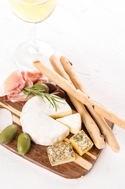 Tahta şarküteri tahtası, zeytin, Grissini ve bir bardak şarapla servis edilen peynir ve jambon seçimi. İtalyan geleneksel antipasti, dikey görüntü