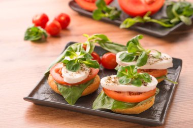Caprese salatası, dilimlenmiş domates, mozzarella, fesleğen ve üzeri siyah tabakta mısır salatası, ahşap masa arkası. Klasik İtalyan marşı.