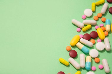 Assorted medicine pills, capsules and tablets on green background with copy space. Immune system vitamins and supplemets. Selective focus