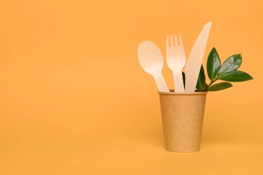 Kağıt bardakta bulunan doğal ahşap bambu çatal bıçak seti. Biyo-çözünebilir ve gübrelenebilir çatal bıçak seti ve sofra takımı konsepti. Fotokopi alanı olan turuncu arka planda bambu çatal bıçak takımı. Çevre koruma kavramı. Model