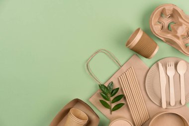 Sustainable food packaging - kraft paper food cups, containers, paper bag, wooden cutlery set and drinking straws on light green background with copy space. Street food take away paper utensils. Flat lay