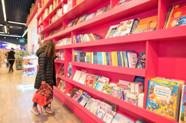 Lviv, Ukrayna - 7 Mayıs 2022: Oyuncak Evi 'nde çeşitli çocuk kitapları bulunan raflar, en büyük oyuncak mağazası. Oyuncakçıda doğum günü hediyesini seçen genç bir kadın. Seçici odak