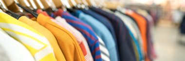 Askıda giysileri olan afiş. Moda mağazasında yeni moda koleksiyonu. Kıyafet kiralama ya da satış konsepti. Giysiler kopya alanı ile bulanık depolama arka planına karşı dururlar