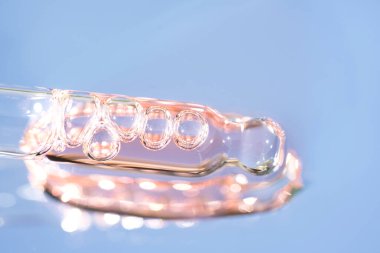 Mavi cam zemin üzerinde pembe kozmetik sıvıyla fotokopi alanı olan bir boru. Yüz serumu veya kozmetik yağ dokusu. Seçici odak