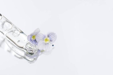 Beyaz cam zemin üzerinde şeffaf sıvıyla fotokopi alanı olan bir boru. Yüz serumu veya kozmetik yağ dokusu. Seçici odak, makro fotoğraf