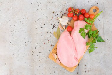 Tahta kesme tahtasının üzerinde taze çiğ tavuk filetosu, baharatlar ve domatesler. Beton masa arkasında pişmemiş tavuk göğsü ve fotokopi alanı. Gıda arkaplanı