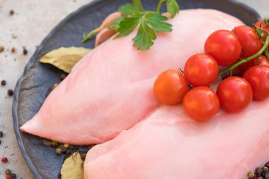 Siyah tabakta çiğ tavuk filetosu, baharat ve domates. Beton masa arkasında pişmemiş tavuk göğsü. Gıda arkaplanı