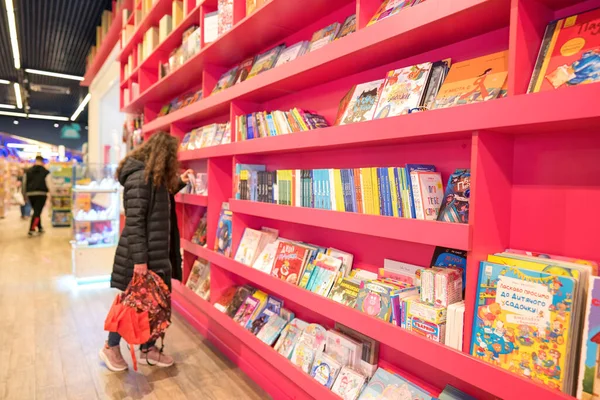 Lviv, Ukrayna - 7 Mayıs 2022: Oyuncak Evi 'nde çeşitli çocuk kitapları bulunan raflar, en büyük oyuncak mağazası. Oyuncakçıda doğum günü hediyesini seçen genç bir kadın. Seçici odak