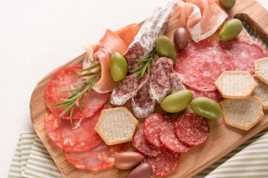 Beyaz beton masa arka planında geleneksel İtalyan antipastisi. Farklı türde sosislerle ahşap şarküteri - salam, bresaola, zeytin ve krakerle servis edilen proscuitto