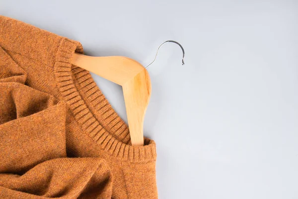 Wooden hangers with orange sweater over gray background with copy space. Clothing donations, conscious and environmentally friendly consupmtion - new trends in shopping, slow fashion concept