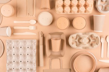  Kağıt çatal bıçak takımı, ahşap çatal bıçak takımı, kağıt bardak, tabak, torba, yumurta kutusu ve açık kahverengi arka planda yiyecek kapları. Üst Manzara. Sürdürülebilir gıda paketleme kavramı