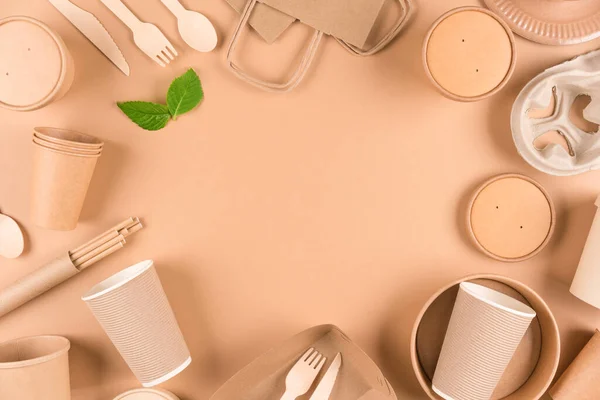 Sustainable food packaging concept - kraft paper utensils, wooden cutlery set, paper cups, plates, bags and food containers over light brown background with copy space. Top view