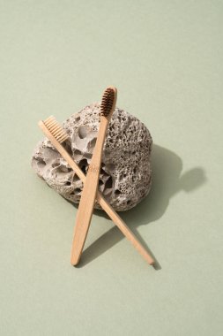 Doğal ahşap bambu diş fırçaları ve zeytin yeşili arka planda doğal taşla dikey bileşim. Model resmi
