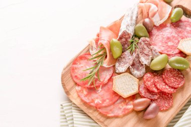 Geleneksel İtalyan antipastisi beyaz masa üzerinde. Farklı türde sosislerle ahşap şarküteri tahtası. Salam, bresaola, zeytin ve krakerle servis edilen proscuitto. Kopyalama alanı olan menü arkaplanı