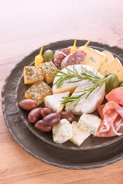 Vertical image with cheese plate - selection of cheeses, sausages and prosciutto served with olives and herbs on white table background with copy space. Cheese plate for aperitif, happy hour menu. Italian antipasti