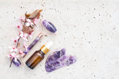 Yüz masajı kiti ile düz kompozisyon - ametist gua sha aracı ve yüz silindiri ile güzellik yüz serumu ya da taş beton arka planda fotokopi alanı ile kozmetik yağ. Model görüntü, cilt bakımı konsepti 