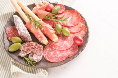 Farklı sosislerle servis edilen şarküteri tabağı - salam, bresaola, proscuitto ve Grissini ekmek çubukları. Menü arka planı. Beyaz masada geleneksel İtalyan antipastisi.