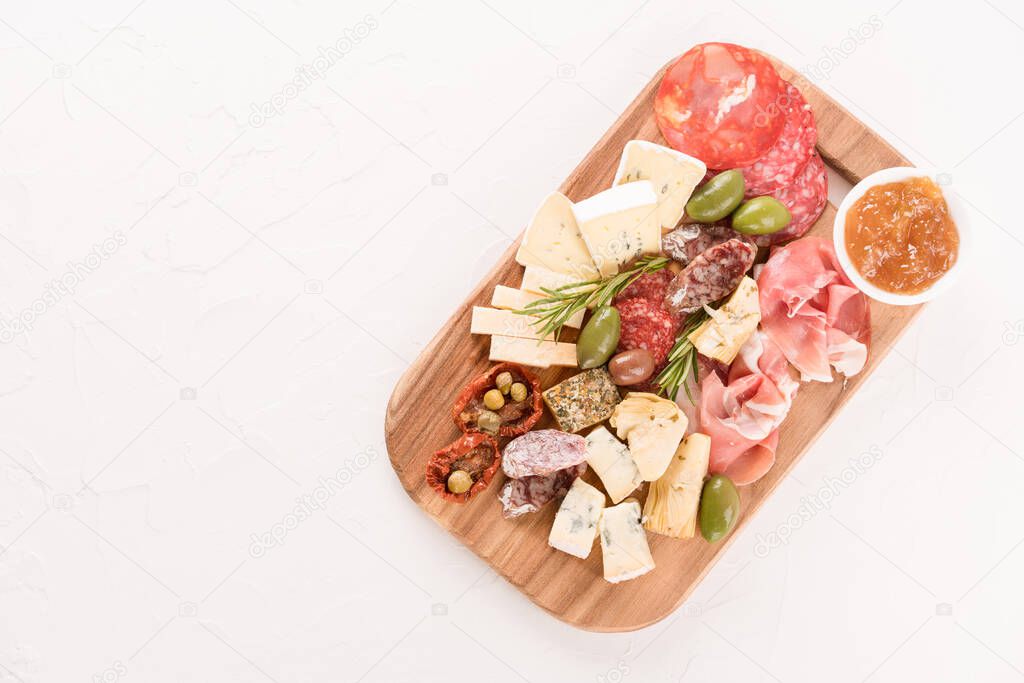 Italian antipasti board with variety of cheeses, sausages served with sun dried tomatoes, olives, jams and herbs at white table - parmesan, dorblu, prosciutto, salami. Cheese and meat snacks platter.  Copy space