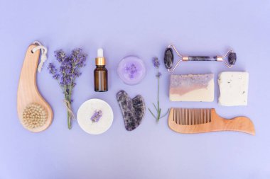 Doğal banyo aksesuarları ve ev vücudu ve cilt bakımı için eflatun çiçekleri ile mor arkaplan üzerinde doğal bakım ürünleri. Doğal bitkisel lavanta kozmetik seti, ekolojik yaşam konsepti. Düzleştirme biçimi