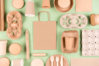 Eco tableware, paper utensils and wooden bamboo cutlery set over light green background. Flat lay style. Sustainable food packaging concept