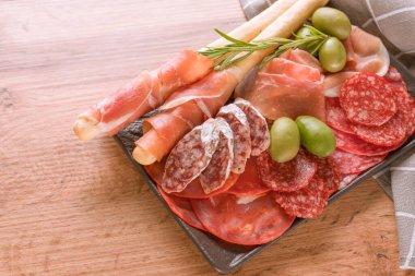 Farklı sosislerle servis edilen şarküteri tabağı - salam, bresaola, proscuitto ve Grissini ekmek çubukları. Menü arka planı. Ahşap masada geleneksel İtalyan antipastisi.