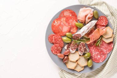 Sosis çeşitleri ile şarküteri tabağı - salam, bresaola, zeytinli proscuitto ve beyaz masanın üzerinde kraker. Kopyalama alanı olan menü arkaplanı. Geleneksel İtalyan antipatisi