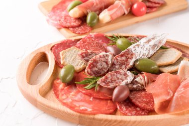 Sosis çeşitleri olan şarküteri tahtası - salam, bresaola, zeytin ve beyaz masanın üzerinde krakerle servis edilen proscuitto. Kopyalama alanı olan menü arkaplanı. Geleneksel İtalyan antipatisi
