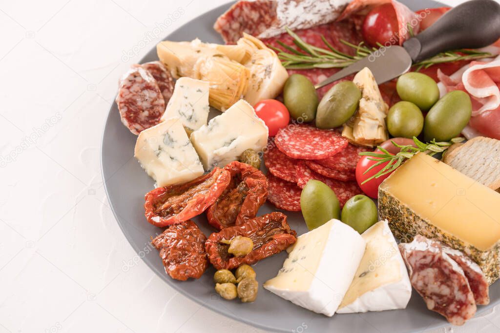 Italian antipasti plate with variety of cheeses, sausages served with sun dried tomatoes, olives and herbs on wooden table. Cheese and meat snacks platter.  Menu background