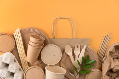 Eco-friendly paper utensils - kraft paper food packaging over orange background with copy space. Street food paper packaging, recyclable tableware, zero waste packaging concept