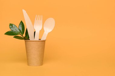 Kağıt bardakta bulunan doğal ahşap bambu çatal bıçak seti. Biyo-çözünebilir ve gübrelenebilir çatal bıçak seti ve sofra takımı konsepti. Bambu çatal bıçak takımı turuncu arka plana karşı fotokopi alanı ile. Çevresel koruma