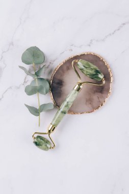 Beyaz mermer masa arka planında yüz masajı için yeşim yüzlü gua sha. Doğal taşlardan yapılan yüz masajı aletleri. Cilt bakım aletleri. Seçici odak, dikey resim