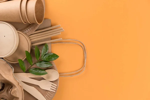 Kraft paper food cups, containers, wooden cutlery set, drinking straws and paper bag over orange background with copy space. Street food take away paper utensils. Selective focus