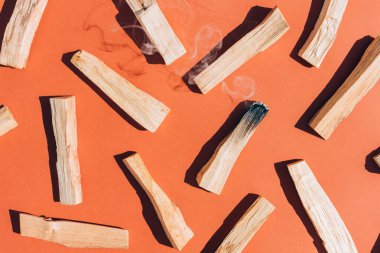 Burning incense - palo santo sticks over orange brown background, Earth tone. Flat lay composition with holy wood sticks for meditation and spiritual practices. Room fumigation ritual. Selective focus