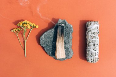 Yanan tütsü - beyaz adaçayı ve palo santo, kahverengi arka planda taş üstünde dumanla yapışır. Meditasyon ve oda ilaçlaması için demet. Seçici odaklanma. Düzleştirme biçimi