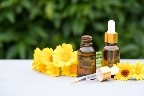 Concept of making natural cosmetics at home - dropper bottles with calendula oil against green leaves as natural background. Herbal cosmetic oil for skincare or essential oil for aromatherapy. Mockup image