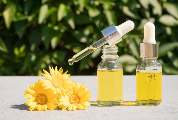Making natural herbal cosmetics at home - dropper bottles with calendula oil against green leaves as natural background. Herbal cosmetic oil for skincare or essential oil for aromatherapy. Mockup image